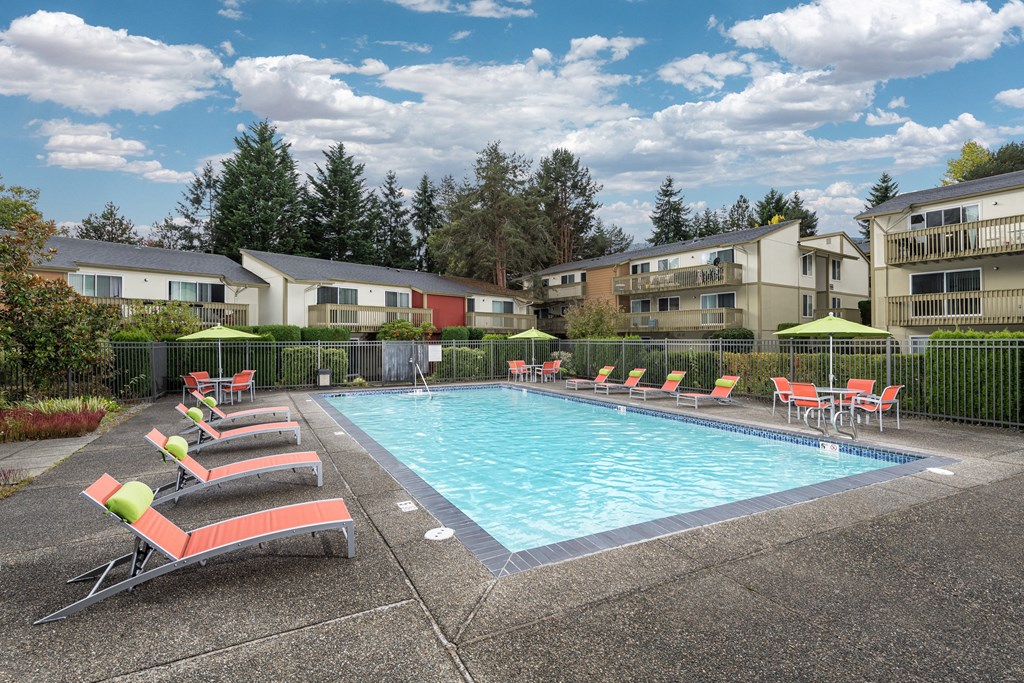 A pool surrounded by chairs and trees.